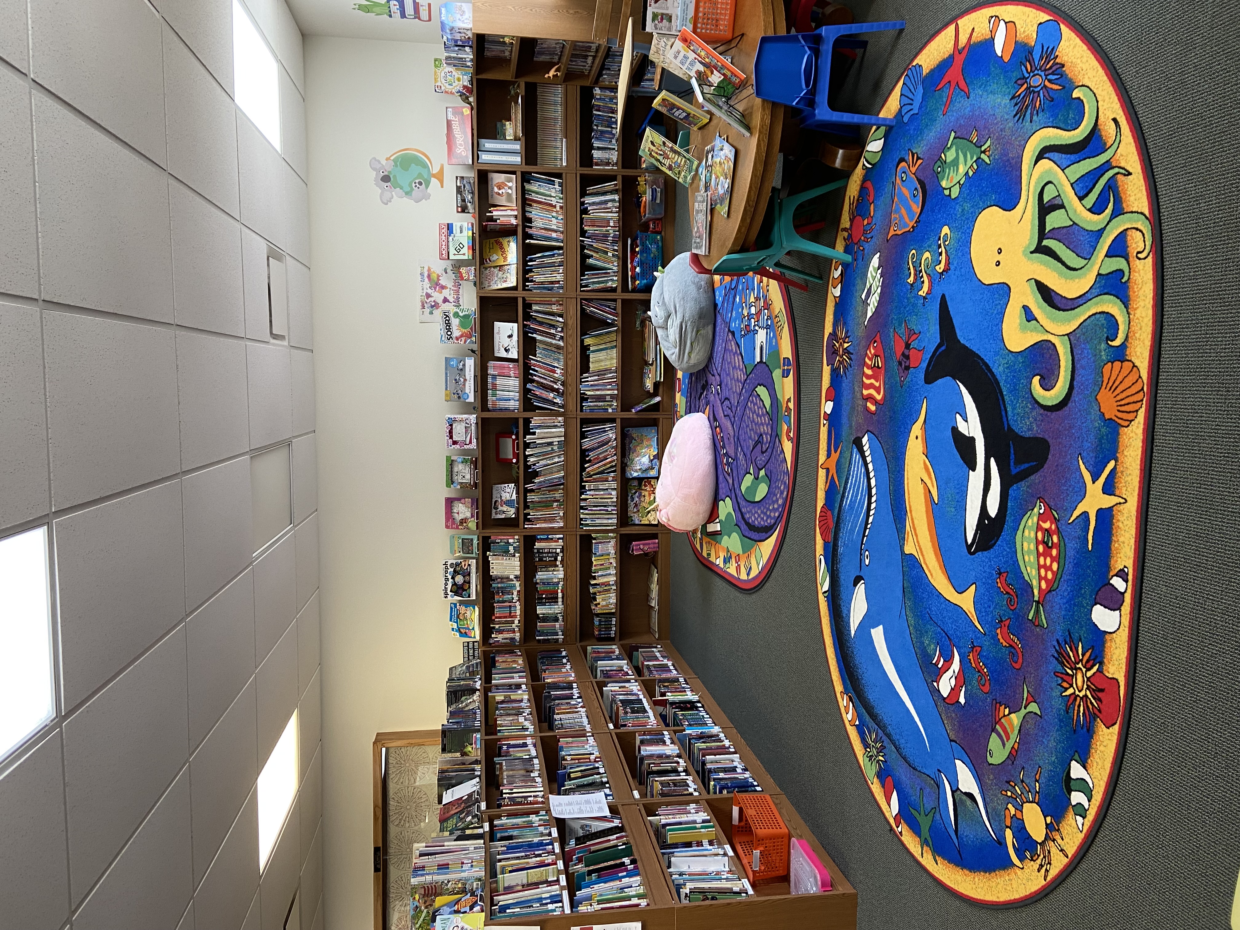 Children's area of the library with blue ocean themed rug, children's table and bookshelves.